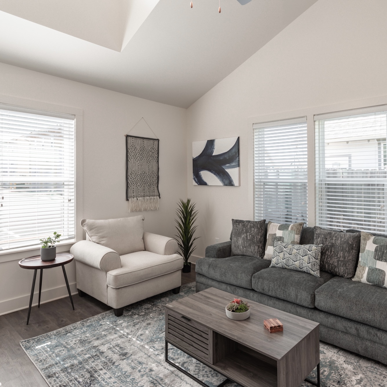Spacious Apartment Living Room with Tall Ceilings Apartment living room with tall ceilings, neutral color scheme, multiple windows, coffee table, sofa, armchair, end table, and house plants in Madison, AL.